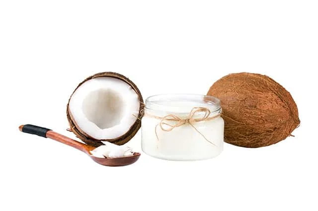 A Cup of virgin coconut oil and scoped spoon with few coconuts